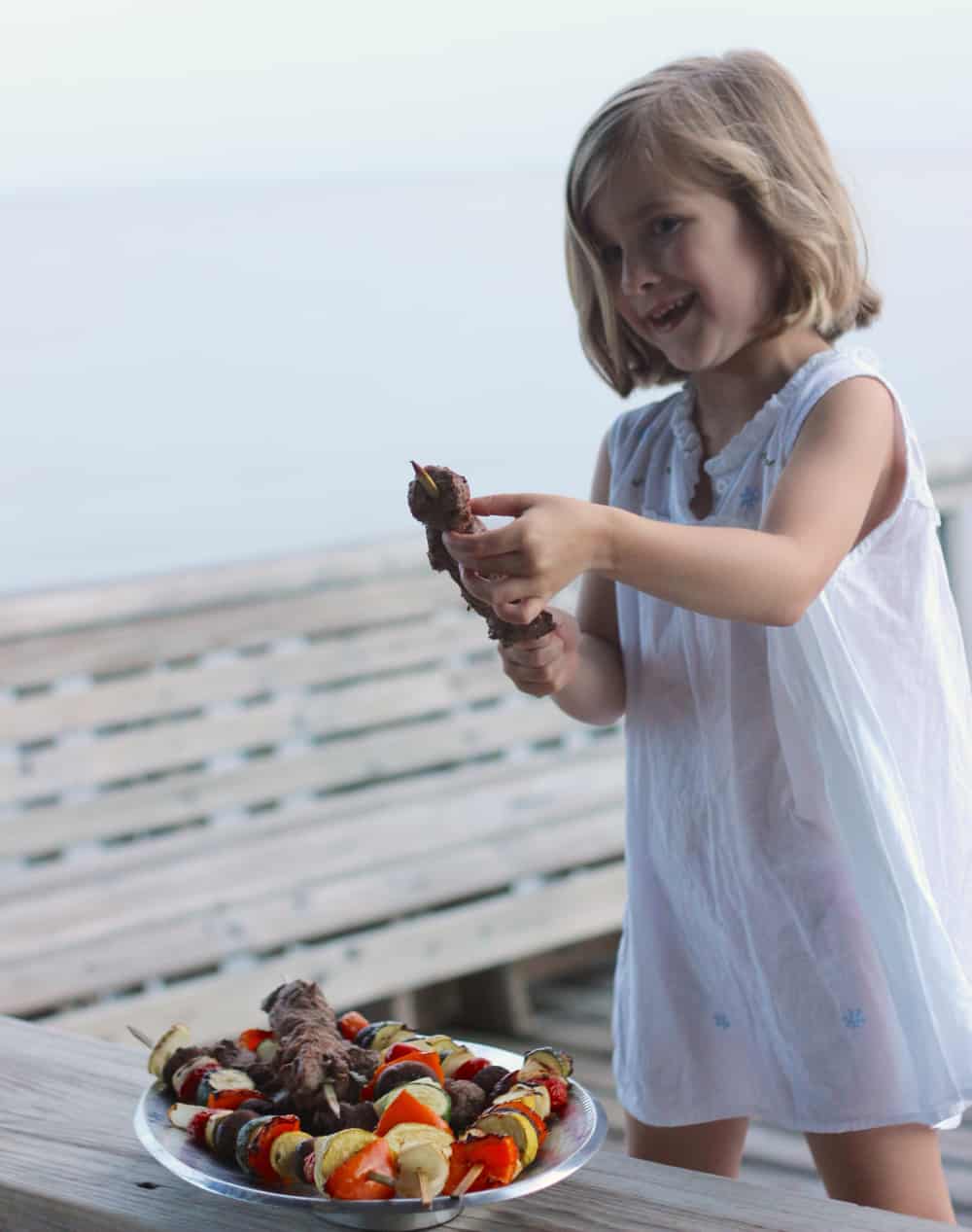 little girl smiling and taking lamb off a skewer
