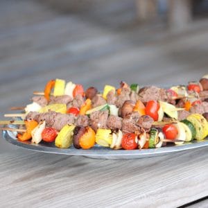 silver platter on wooden pier with vegetable and lamb kabobs
