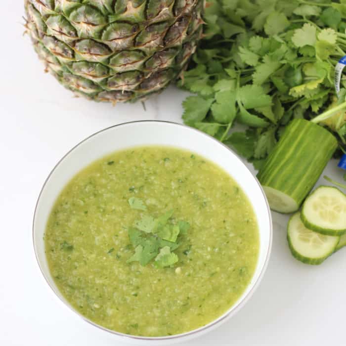 pineapple cucumber gazpacho in a white bowl with whole pineapple, cilantro, sliced cucumber