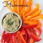 bowl of eggplant hummus with parsley on top surrounded by sliced red and orange bell peppers