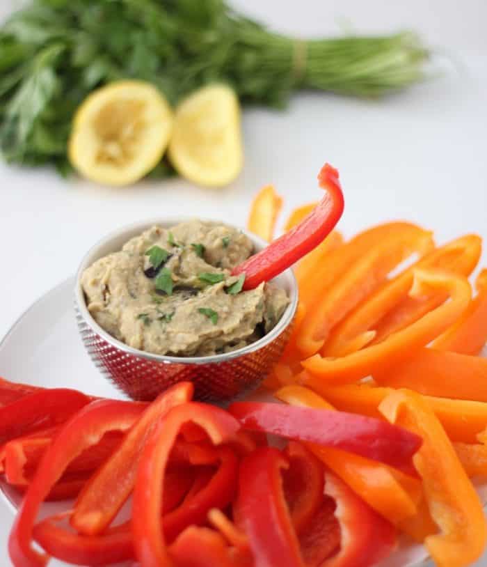 roasted eggplant hummus in a small gold bowl with a red bell pepper sticking out of hummus, lemon, parsley, bell peppers