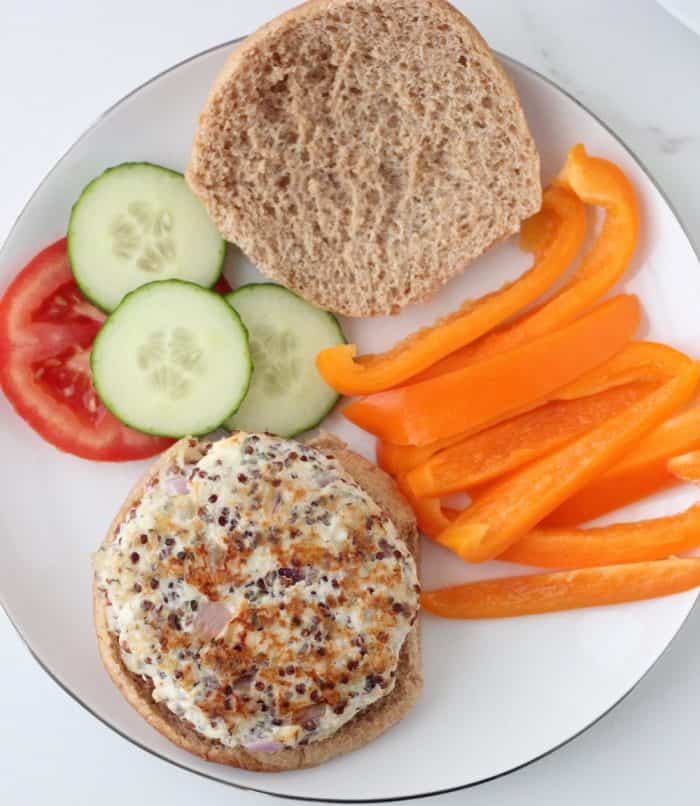 Greek Turkey Quinoa Burgers on a hamburger bun on plate with bell peppers, cucumber, tomatoes