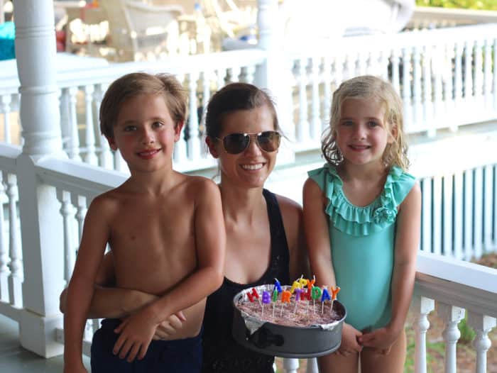 young boy and girl in bathing suits hugging a brunette female adult holding ice cream cake on a white porch