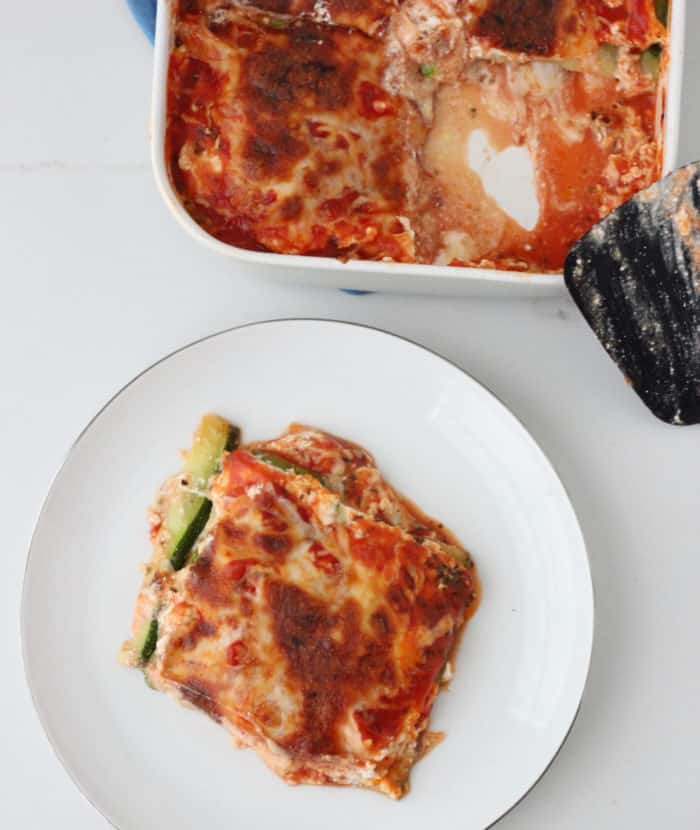 white plate with slice of Zucchini Lasagna with a casserole dish of lasagna and spatula