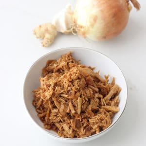 bowl of garlic ginger pork next to a yellow onion, fresh garlic and ginger.