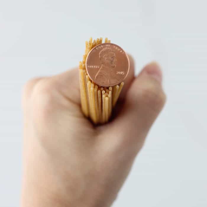 hand holding pasta with a penny on top