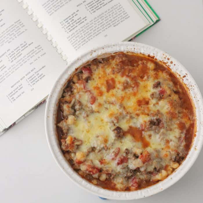 open cookbook with a white casserole dish filled with beef, tomatoes, and hominy covered in cheese