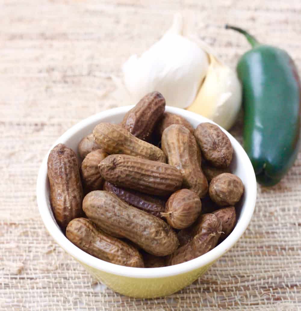 yellow bowl with boiled peanuts, head of garlic, and a jalapeno on a straw placemat