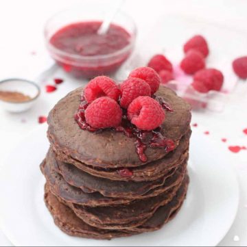 stack of chocolate protein pancakes with raspberries and raspberry sauce on top and in background