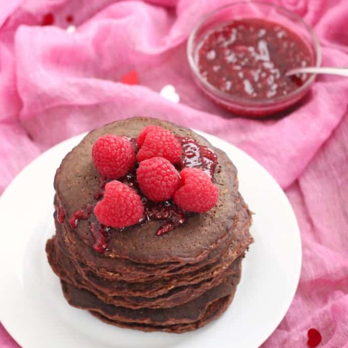 Chocolate Protein Pancakes with raspberries and raspberry sauce on pink towel with heart confetti 