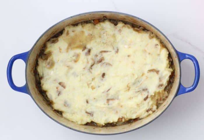 blue dutch oven with casserole covered in mashed potatoes