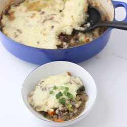 blue pot of shepherd's pie with black spoon and a small white bowl with casserole