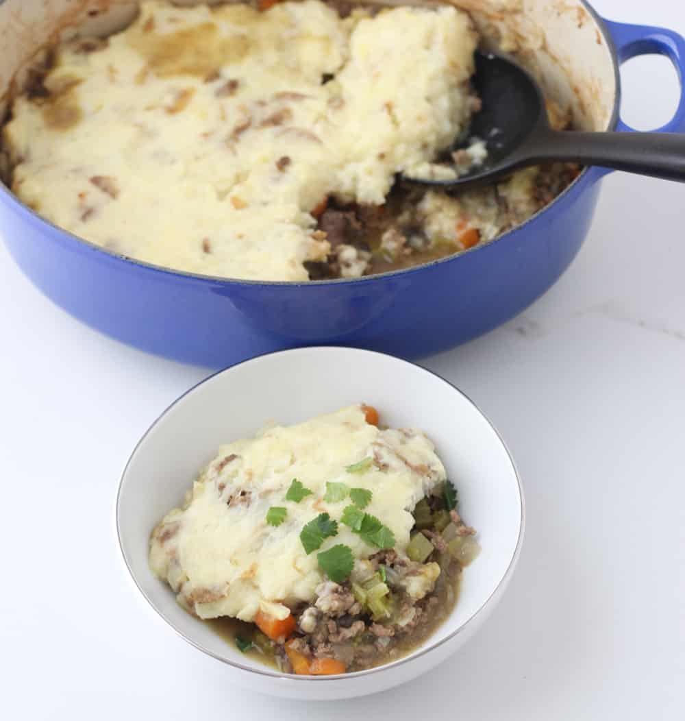 blue pot of shepherd's pie with black spoon and a small white bowl with casserole