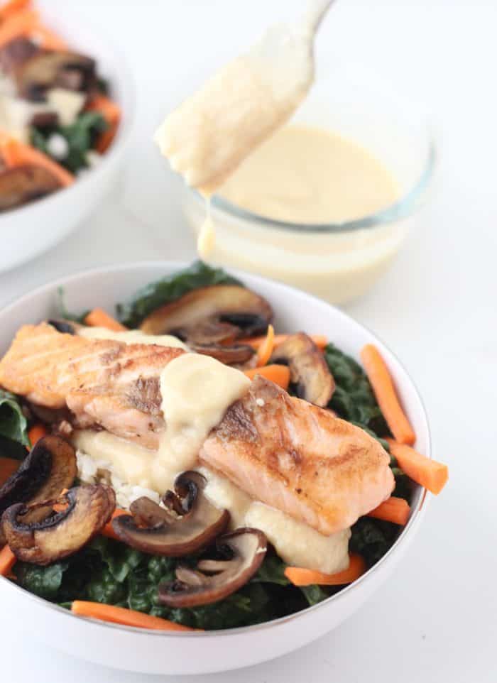 Miso Dressing drizzled from a fork onto a bowl of salmon, kale, mushrooms, carrots and brown rice