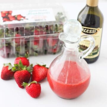 fresh strawberries on white counter with glass container of strawberry dressing, jar of balsamic vinegar