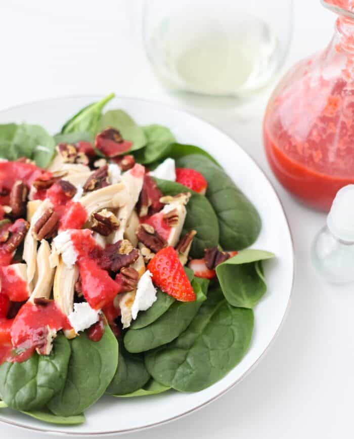 plate of spinach, pecan and goat cheese salad covered in strawberry salad dressing with a glass of white wine