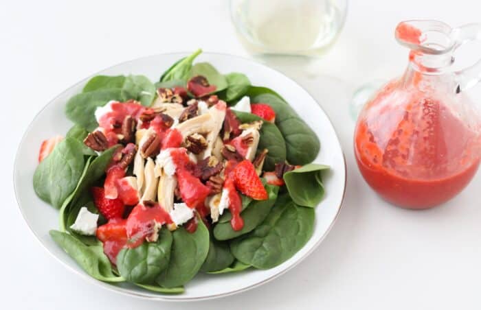 bottle of salad dressing, plate of spinach salad with pecans, feta and strawberries