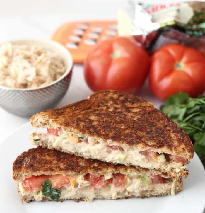 Chicken Salad Grilled Cheese on white plate with tomatoes, chicken salad, cheese grater, parsley