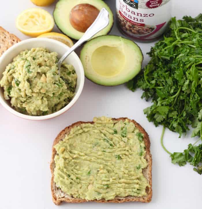 slice of avocado toast with a bowl of mashed chickpeas and avocado, cilantro, chickpeas