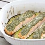 salmon fillets covered in pesto in a white baking dish on wooden table