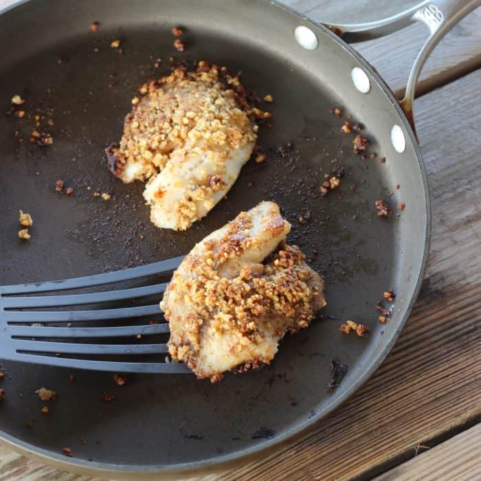 spatula lifting Walnut Crusted Fish out of a skillet on wooden table