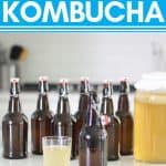 bottles of kombucha on white counter with glass of kombucha in clear glass