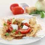 plate of Tomato Basil Nachos with tomatoes, cheese and basil in background