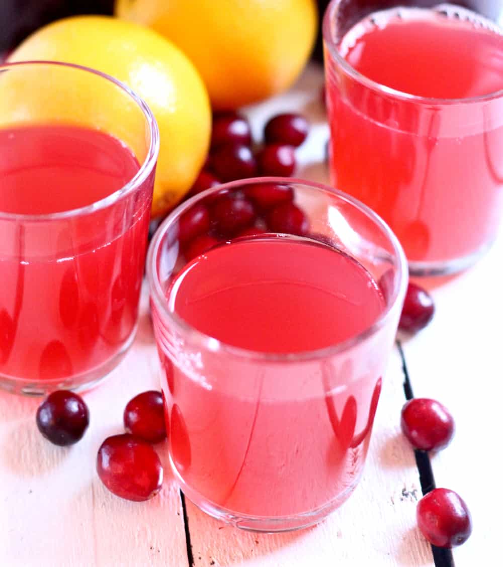 small glasses of cranberry orange kombucha with oranges and fresh cramberries