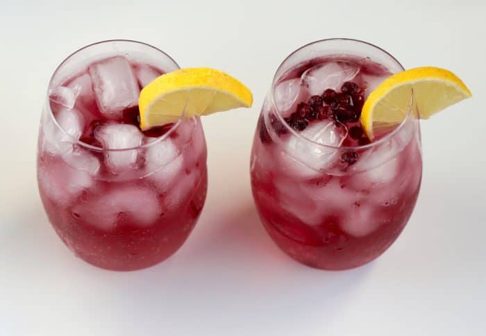 two wine glasses filled with a blueberry lemon cocktail with lemon slices on a white table