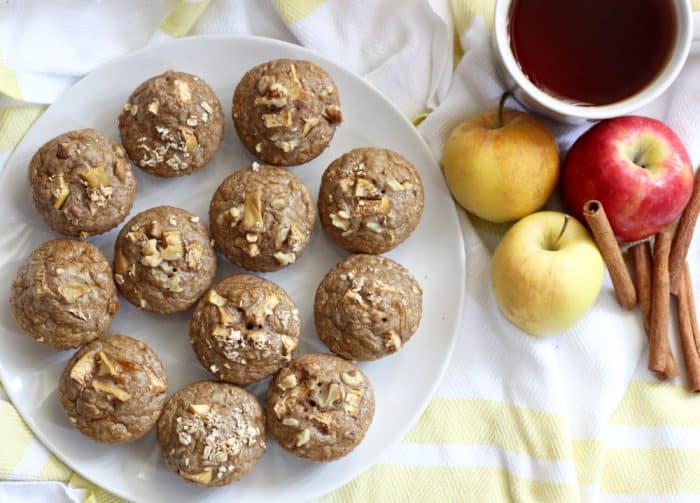 plate of pancake muffins on white and yellow towel with apples, cinnamon sticks and a cup of tea