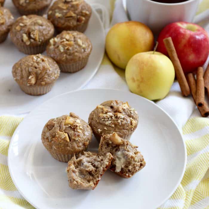 white plates with apple pancake muffins and one broken in half topped with butter. plus apples, cinnamon sticks, and a coffee cup all on a yellow and white towel