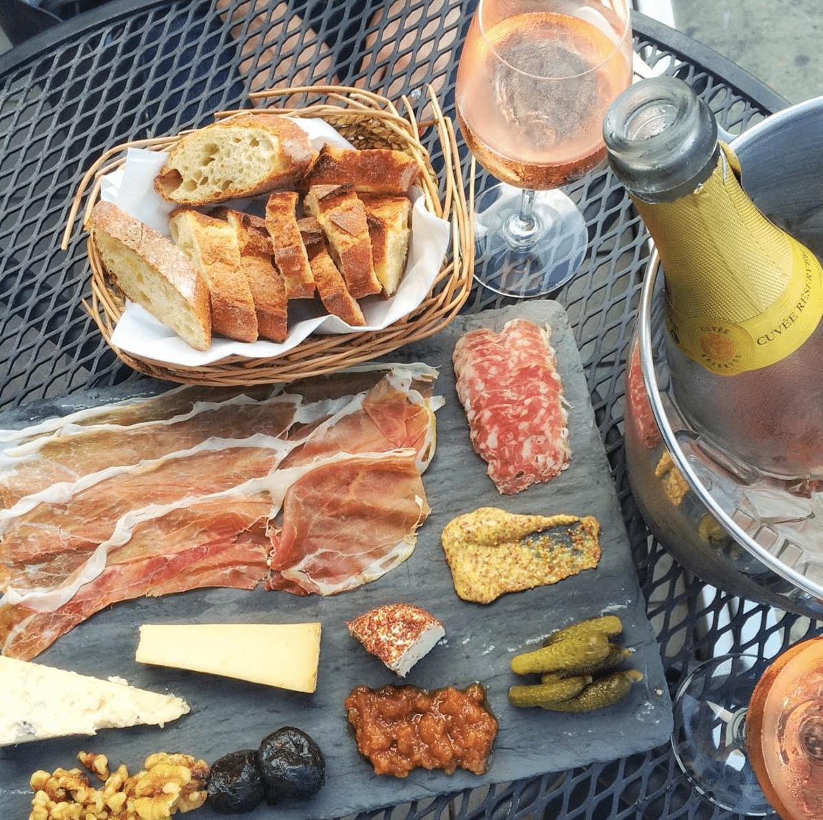 outdoor table with a Cheese plate next to a bucket of sparkling wine.