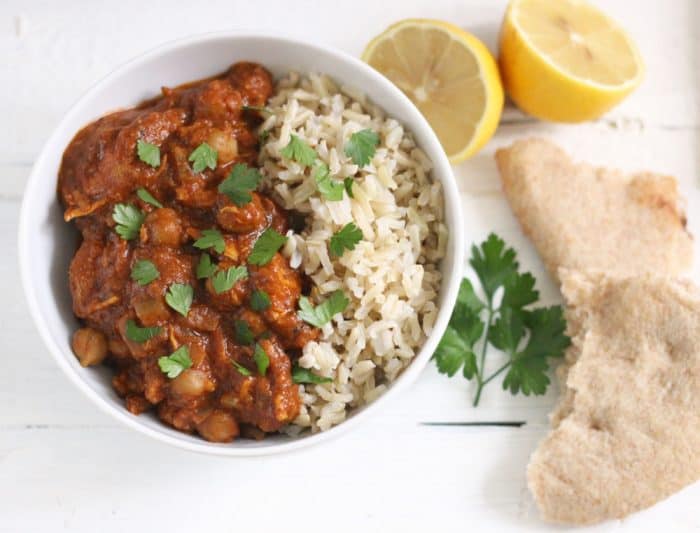 bowl of Chicken Tikka Masala and rice with cut lemon and pieces of naan