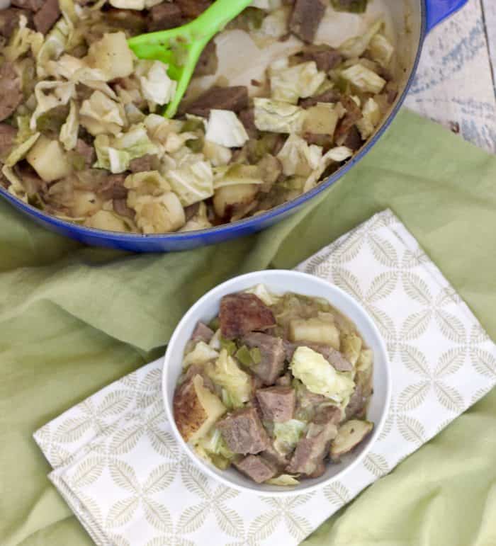 cabbage and corn beef in a white bowl on green and white napkin with pot of hash and green spoon