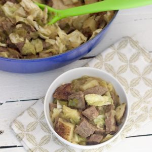 white bowl of corned beef cabbage hash on green and white napkin on a white wooden table with a blue pot