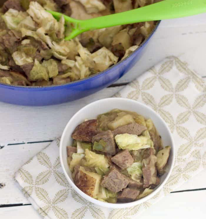 white bowl of corned beef cabbage hash on green and white napkin on a white wooden table with a blue pot