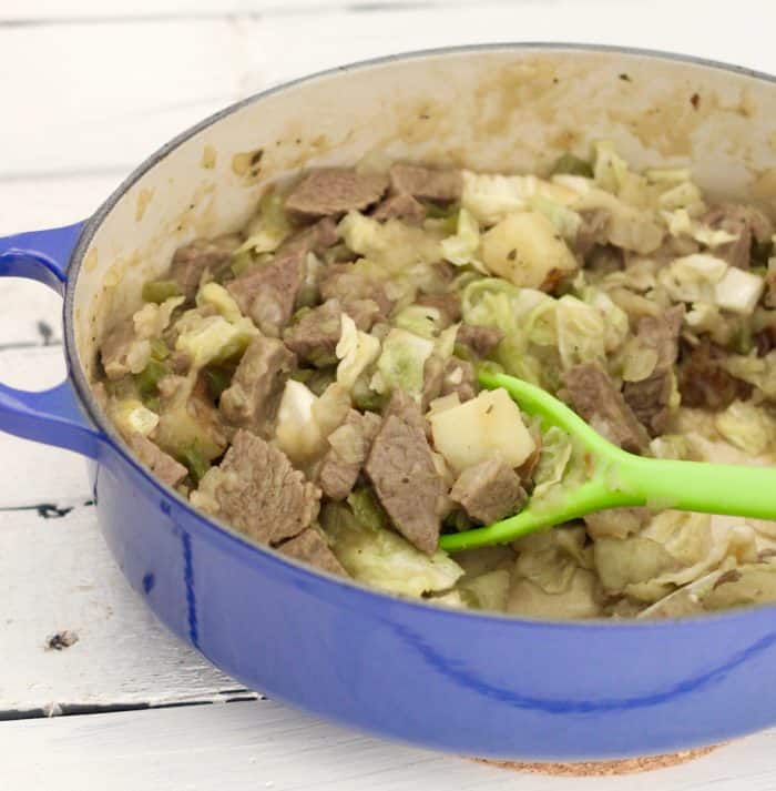 blue pot on white wooden table with corned beef hash and cabbage stirred by a green spoon