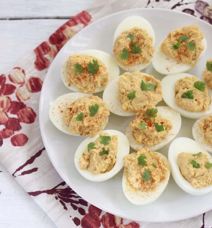 white wooden table with cream and red floral napkin with white plate full of hummus deviled eggs