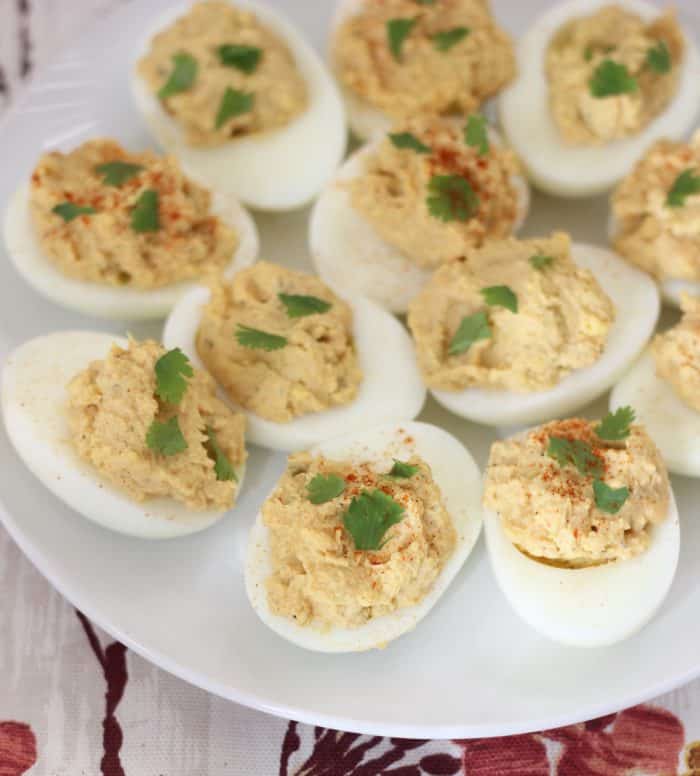 close up photo of deviled eggs on a white plate topped with herbs and paprika