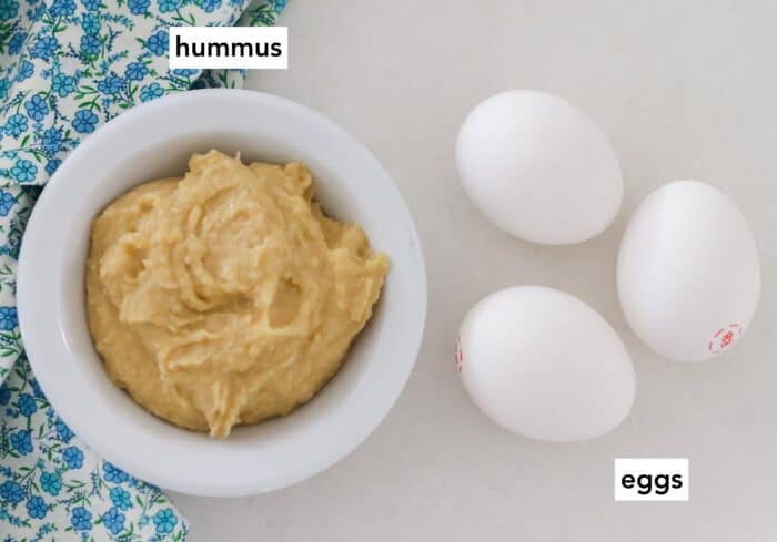 bowl of hummus, 3 eggs on white counter with blue flower napkins