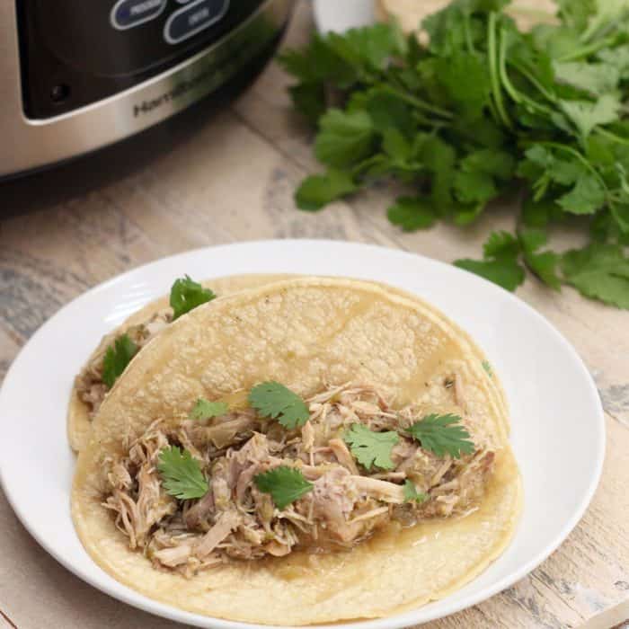 white table with two pork tacos with pork and cilantro on a wooden table