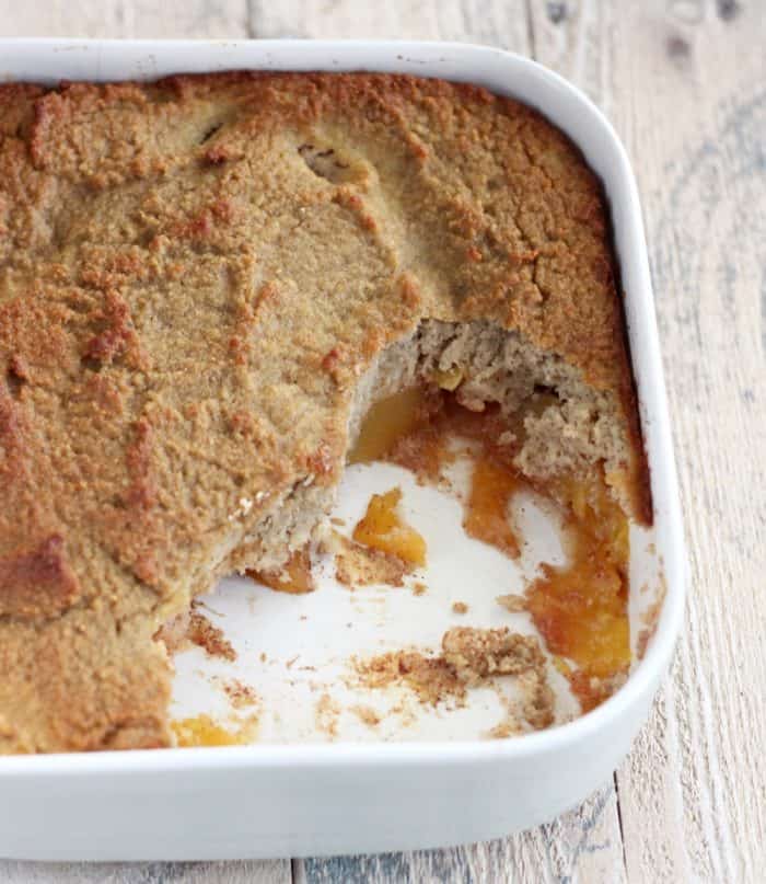 white baking dish with peach cobbler, some scooped out