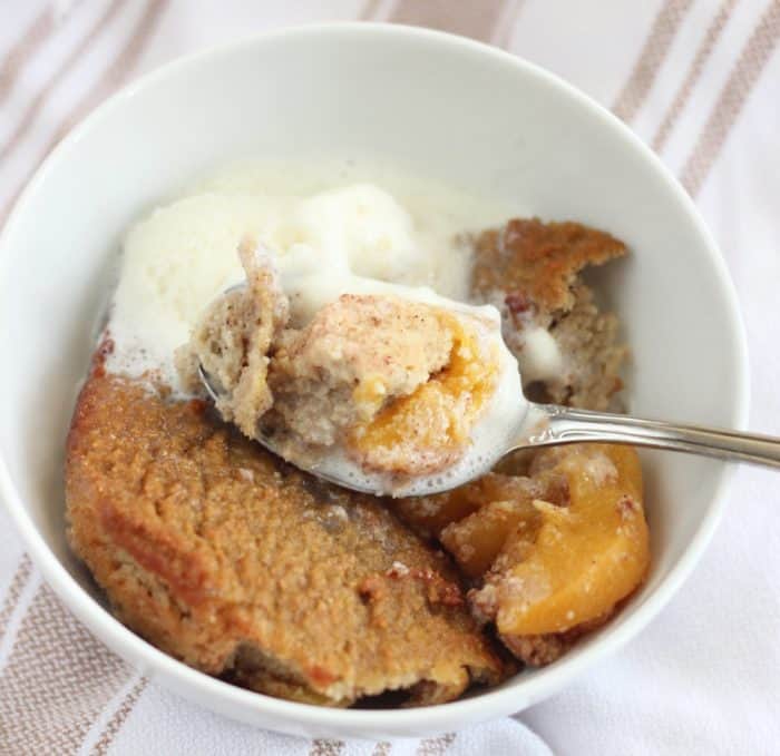 white bowl on brown and white stripe towel with peach cobbler, ice cream, spoon