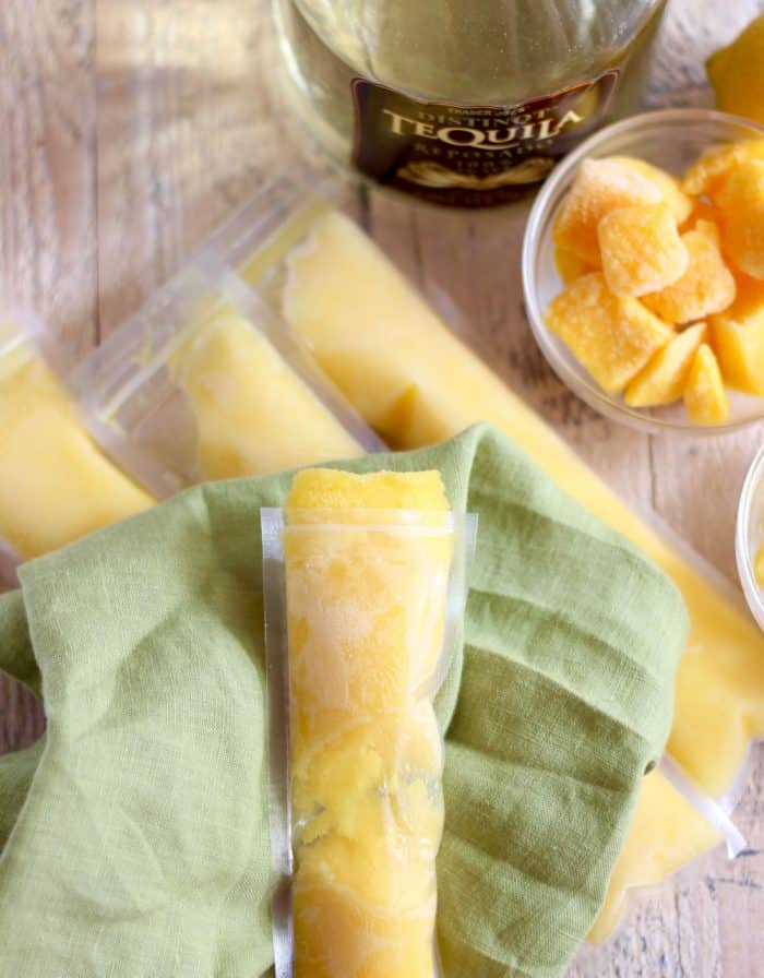 Boozy Mango Pineapple Popsicle on green napkin with other popsicles, tequila, mango