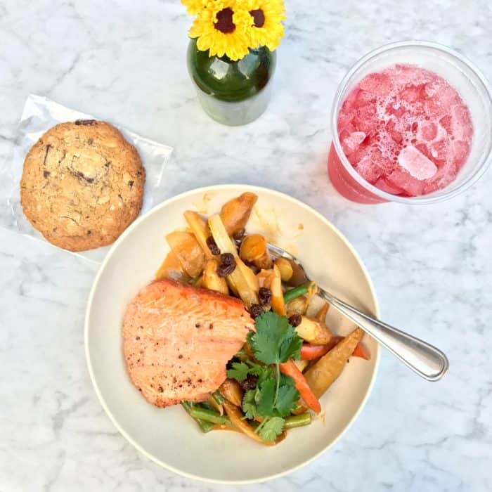 plate of salmon and vegetables on a marble table with an iced hibiscus tea and a chocolate chip cookie