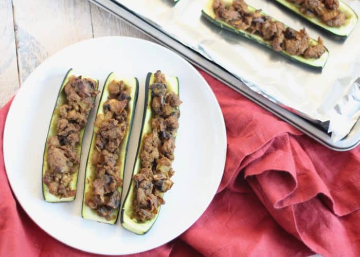 3 stuffed zucchini on white plate on red napkin with baking sheet
