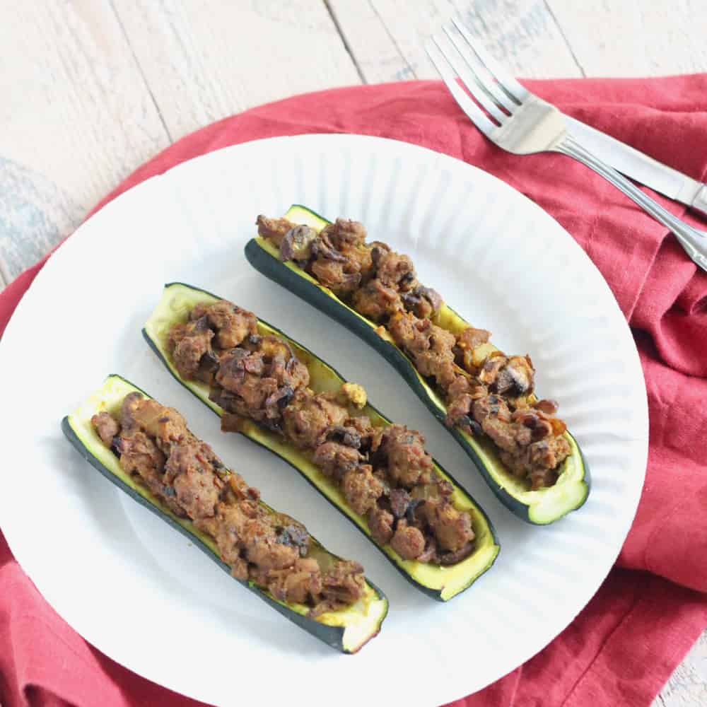 3 Lamb Stuffed Zucchini on a white plate with a red napkin and fork and knife