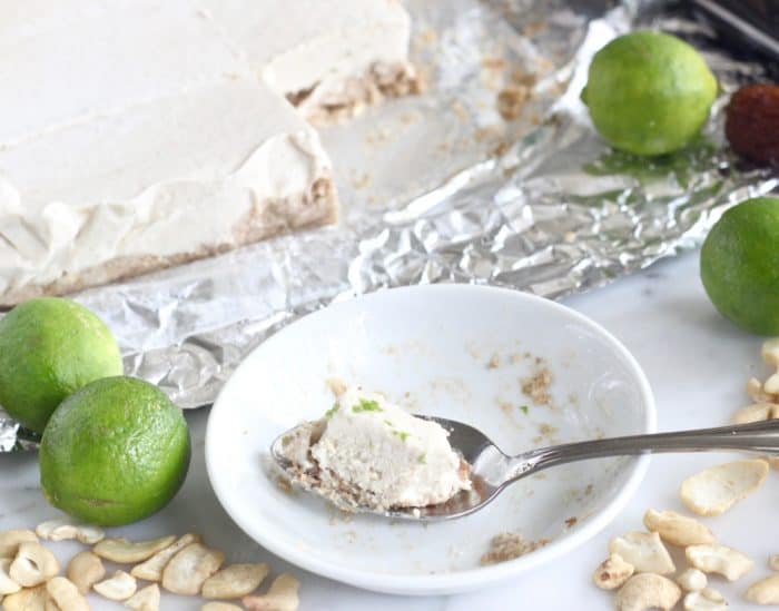 spoon with Key Lime Pie Bar on small white plate, key limes, cashews