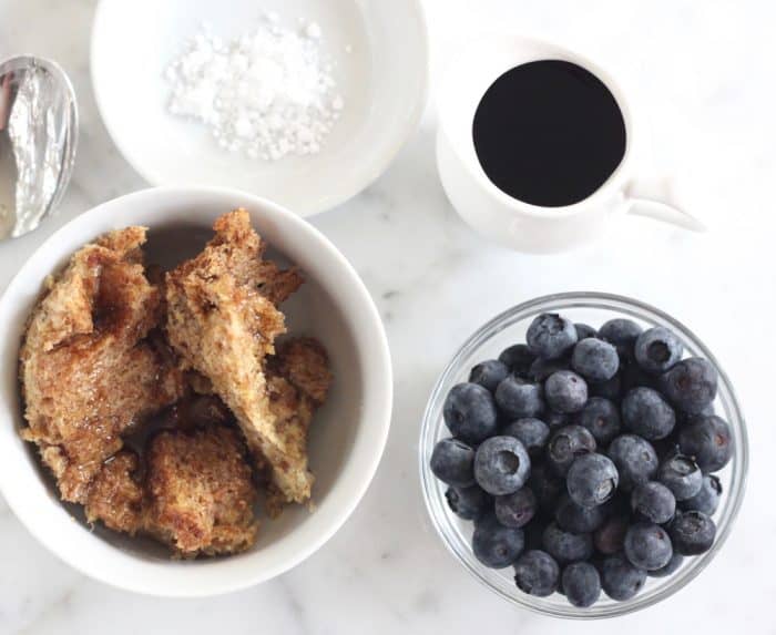 bowl of fresh toast casserole sprinkled with powdered sugar with syrup and blueberries