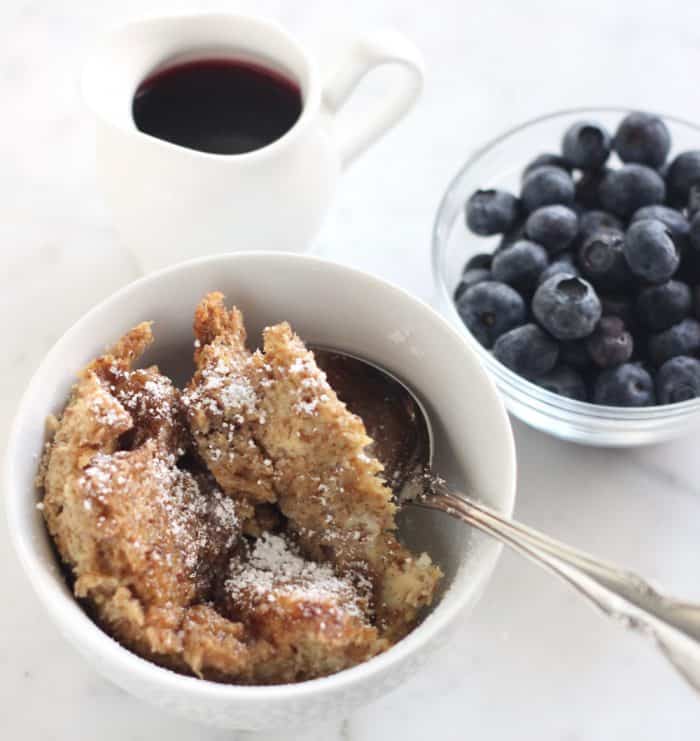 bowl of French Toast Casserole with powdered sugar, syrup, and blueberries